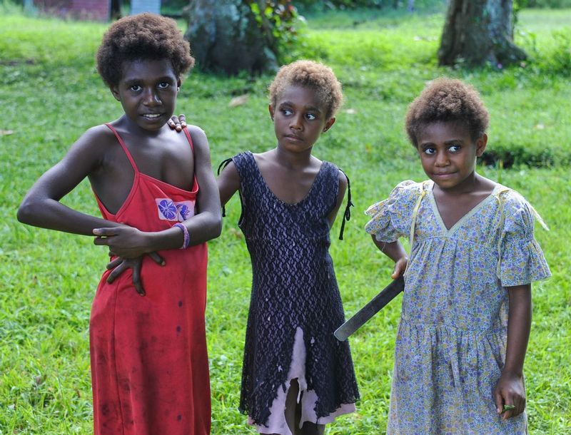 GIRLS OF VUTEKAI.jpg :: VILLAGE OF VUTEKAI.  ISLAND OF PAAMA, VANUATU.  Children of Vanuatu live where there is little influence from the outside world. Responsibility comes at a young age. Very likely, these three young girls already work to contribute to the well-being of their families, helping their mothers cook and care for younger siblings. Notice the machete knife tucked under the arm of one of the girls. This was not an uncommon sight. 

