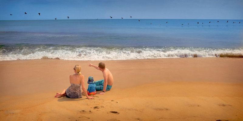 Day At The Beach.jpg :: I love the way the cool blue sky reflecting in the water and the warm golden sand are separated by a thin white line of surf. A couple and their young son enjoying their afternoon on the surf smoothed sand - I wonder if maybe they are trying to get him to say \