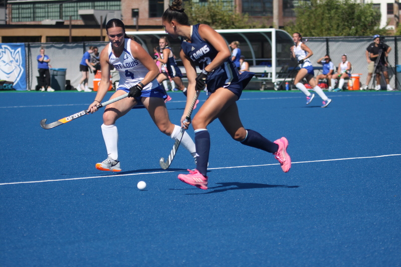 Saint Louis University (SLU) Field Hockey vs UC Davis 2025 LIII.jpg :: SLU Field Hockey vs University of California Davis at the SLU Field Hockey Complex - Women's Field Hockey - The standard field size for field hockey is 300 feet (100 meters) long and 167 feet wide. A field hockey field's boundaries are marked with the end lines going across the width and sidelines going across the length. - The field is divided into quarters by four lines. The 25-yard line are 25 yards from each end line, and the center line runs through the middle of the field. The goalposts are 12 feet wide, 7 feet tall, and 4 feet deep. Each goal post is situated in the center of each end line. - The Striking Circle is a Semi-Circle with a radius of around 48 feet surrounding each goal. - There are always 22 players on the field, 11 from each team. Each team has a goalkeeper and 10 fielders.
