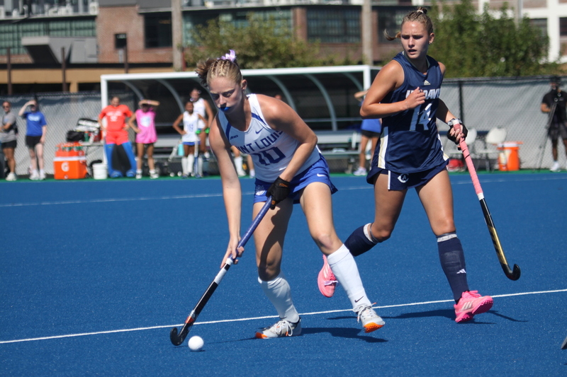 Saint Louis University (SLU) Field Hockey vs UC Davis 2025 XXXIX.jpg :: SLU Field Hockey vs University of California Davis at the SLU Field Hockey Complex - Women's Field Hockey - The standard field size for field hockey is 300 feet (100 meters) long and 167 feet wide. A field hockey field's boundaries are marked with the end lines going across the width and sidelines going across the length. - The field is divided into quarters by four lines. The 25-yard line are 25 yards from each end line, and the center line runs through the middle of the field. The goalposts are 12 feet wide, 7 feet tall, and 4 feet deep. Each goal post is situated in the center of each end line. - The Striking Circle is a Semi-Circle with a radius of around 48 feet surrounding each goal. - There are always 22 players on the field, 11 from each team. Each team has a goalkeeper and 10 fielders.