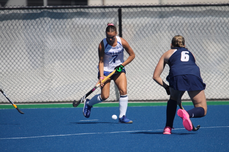 Saint Louis University (SLU) Field Hockey vs UC Davis 2025 XXXVII.jpg :: SLU Field Hockey vs University of California Davis at the SLU Field Hockey Complex - Women's Field Hockey - The standard field size for field hockey is 300 feet (100 meters) long and 167 feet wide. A field hockey field's boundaries are marked with the end lines going across the width and sidelines going across the length. - The field is divided into quarters by four lines. The 25-yard line are 25 yards from each end line, and the center line runs through the middle of the field. The goalposts are 12 feet wide, 7 feet tall, and 4 feet deep. Each goal post is situated in the center of each end line. - The Striking Circle is a Semi-Circle with a radius of around 48 feet surrounding each goal. - There are always 22 players on the field, 11 from each team. Each team has a goalkeeper and 10 fielders.
