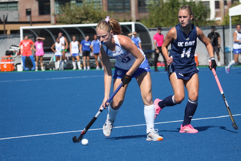 Saint Louis University (SLU) Field Hockey vs UC Davis 2025 XXXX.jpg :: SLU Field Hockey vs University of California Davis at the SLU Field Hockey Complex - Women's Field Hockey - The standard field size for field hockey is 300 feet (100 meters) long and 167 feet wide. A field hockey field's boundaries are marked with the end lines going across the width and sidelines going across the length. - The field is divided into quarters by four lines. The 25-yard line are 25 yards from each end line, and the center line runs through the middle of the field. The goalposts are 12 feet wide, 7 feet tall, and 4 feet deep. Each goal post is situated in the center of each end line. - The Striking Circle is a Semi-Circle with a radius of around 48 feet surrounding each goal. - There are always 22 players on the field, 11 from each team. Each team has a goalkeeper and 10 fielders.