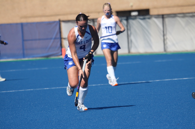 Saint Louis University (SLU) Field Hockey vs UC Davis 2025 XXXXI.jpg :: SLU Field Hockey vs University of California Davis at the SLU Field Hockey Complex - Women's Field Hockey - The standard field size for field hockey is 300 feet (100 meters) long and 167 feet wide. A field hockey field's boundaries are marked with the end lines going across the width and sidelines going across the length. - The field is divided into quarters by four lines. The 25-yard line are 25 yards from each end line, and the center line runs through the middle of the field. The goalposts are 12 feet wide, 7 feet tall, and 4 feet deep. Each goal post is situated in the center of each end line. - The Striking Circle is a Semi-Circle with a radius of around 48 feet surrounding each goal. - There are always 22 players on the field, 11 from each team. Each team has a goalkeeper and 10 fielders.