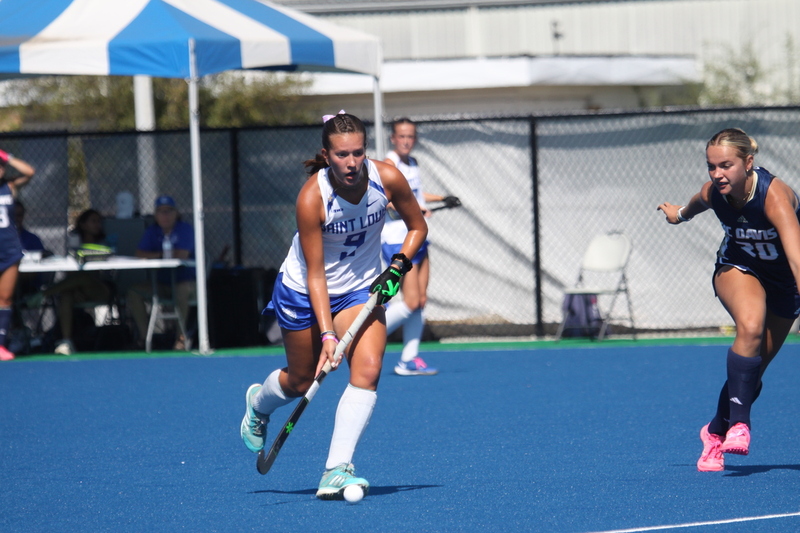 Saint Louis University (SLU) Field Hockey vs UC Davis 2025 XXXXIII.jpg :: SLU Field Hockey vs University of California Davis at the SLU Field Hockey Complex - Women's Field Hockey - The standard field size for field hockey is 300 feet (100 meters) long and 167 feet wide. A field hockey field's boundaries are marked with the end lines going across the width and sidelines going across the length. - The field is divided into quarters by four lines. The 25-yard line are 25 yards from each end line, and the center line runs through the middle of the field. The goalposts are 12 feet wide, 7 feet tall, and 4 feet deep. Each goal post is situated in the center of each end line. - The Striking Circle is a Semi-Circle with a radius of around 48 feet surrounding each goal. - There are always 22 players on the field, 11 from each team. Each team has a goalkeeper and 10 fielders.