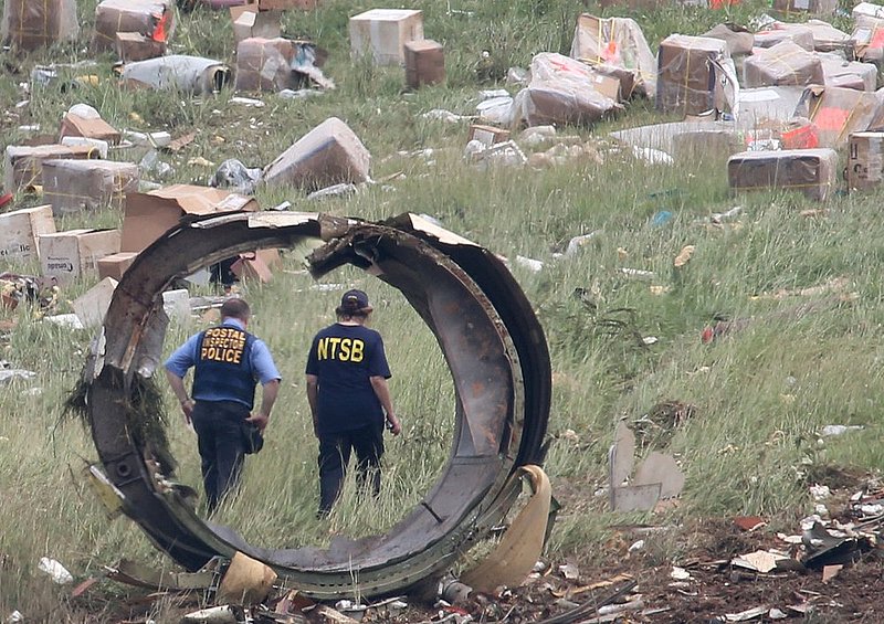 ALHY 114.jpg :: A postal Inspector officer and a NTSB investigator are seen through a section debris of a UPS A300 cargo plane after it crashed on approach at Birmingham-Shuttlesworth International Airport  this morning Wednesday August 14,  2013 in Birmingham, Ala. (AP Photo/Hal Yeager)
