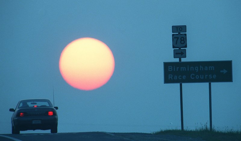 OZONE SUNSET.jpg :: A LONE CARS STOPS AT THE END OF A RAMP FROM I-20 WEST TO HIGHWAY 78 AND THE TURN TO THE BHAM RACE COURSE. WITH THE RECENT ACCUMULATION OF SMOG IN THE BHAM AREA,  PROMPTING AN OZONE ALERT,  THE SUN SEEMS TO GROW LARGER AS IT SETS IN THE AFTERNOON.     