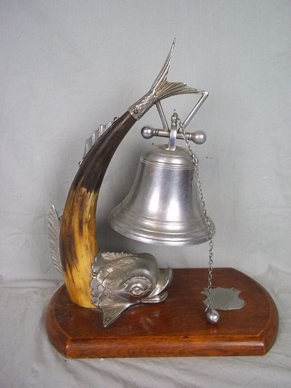 Dolphin Table Bell.jpg :: A silver plate on brass with cow horn dolphin supports the large single bell. The piece is stamped to the dolphin's fin with the maker's mark 'T.W' for Thomas White. The plated bell, either bronze or brass, has a side drawer chain to ring the bell. It rests on an oak stand with an un-engraved metal plaque, which in turns rests on a black marble presentation stand.
This type of stylized dolphin is of a form often used by the British Royal Navy.
$995.00 R14,500 
