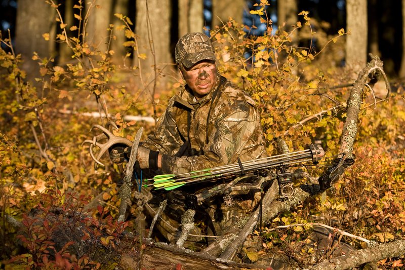 ©TC-Bowhunter-D90010-00627.jpg :: Bowhunter (wearing Advantage AP Brown Camo carrying a Hoyt Compound Bow) crouched down in deadfall and brush rattling for whitetails