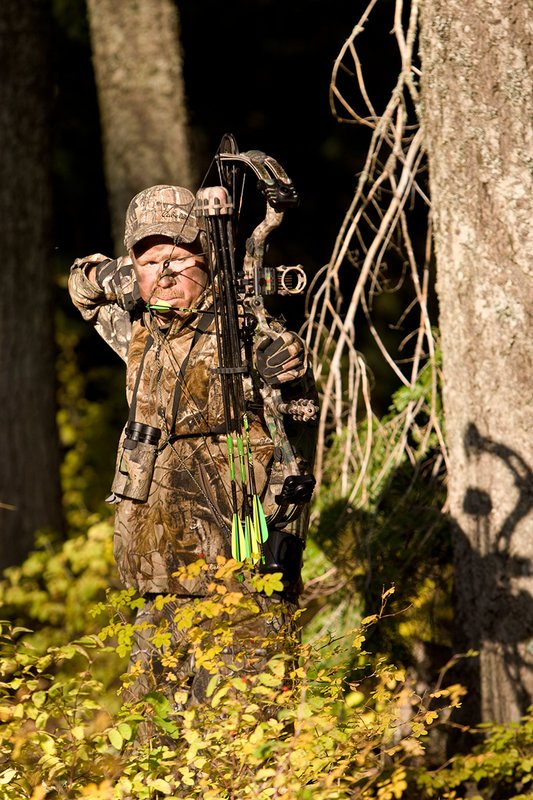 ©TC-Bowhunter-D90010-00639.jpg :: Bowhunter (wearing Advantage AP Brown Camo carrying a Hoyt Compound Bow) at full draw in timber and brush