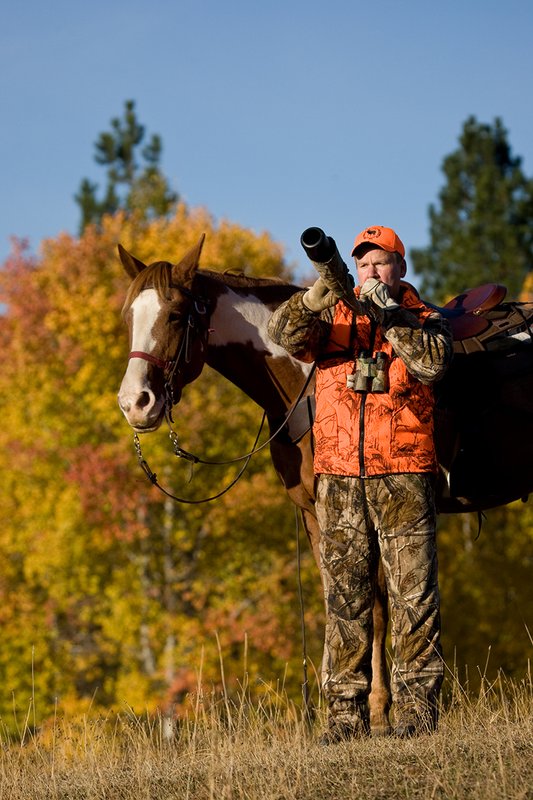 ©TC-Hunter Horseback-D89994-00549.jpg :: Rifle Hunter wearing Advantage HD Brown Camo w/Realtree camo florscent ornage vest/Rocky Mountain Elk Foundation Orange hat bugles for elk while horse stands near him with the backdrop of aspens in golden fall colors