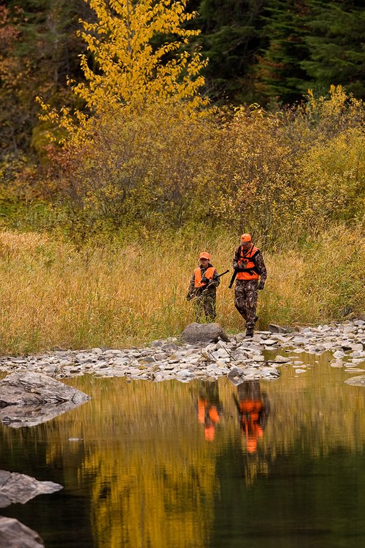 ©TC-Hunter Parent Child-D89995-00042.jpg :: Father wearing Advantage Max 4 camo w/florescent orange vest & hat hunts with his son wearing Realtree Brown camo and florescent orange vest/hat hunt along a river backwater in fall colors