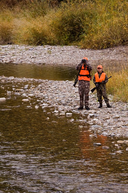 ©TC-Hunter Parent Child-D89995-00059.jpg :: Father wearing Advantage Max 4 camo w/florescent orange vest & hat hunts with his son wearing Realtree Brown camo and florescent orange vest/hat along a river in fall colors