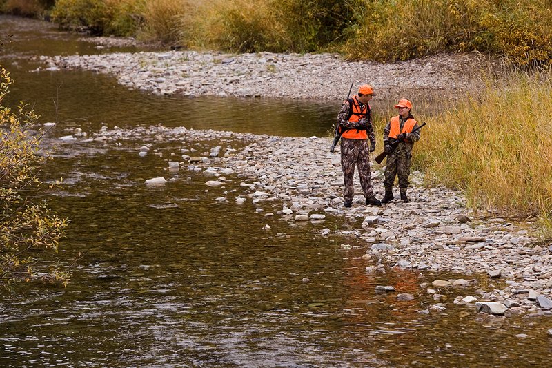 ©TC-Hunter Parent Child-D89995-00060.jpg :: Father wearing Advantage Max 4 camo w/florescent orange vest & hat hunts with his son wearing Realtree Brown camo and florescent orange vest/hat along a river in fall colors