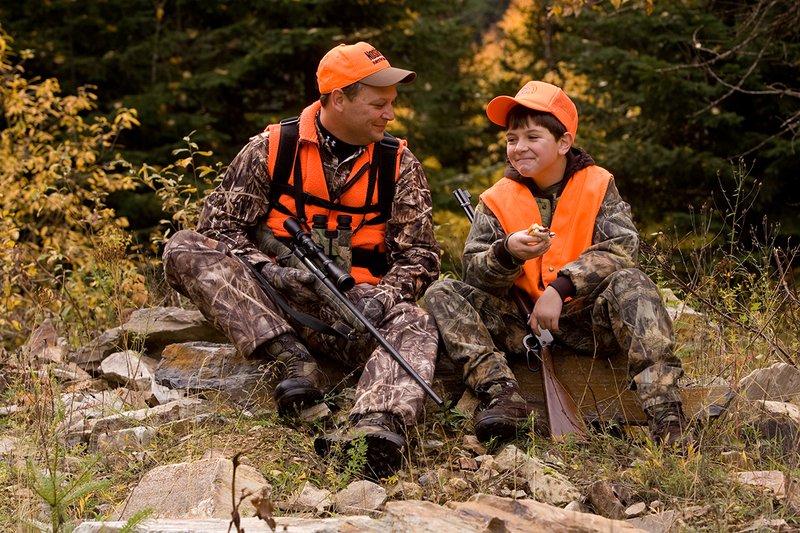 ©TC-Hunter Parent Child-D89995-00080.jpg :: Father wearing Advantage Max 4 camo w/florescent orange vest & hat hunts with his son wearing Realtree Brown camo and florescent orange vest/hat sitting together while on a hunt sharing conversation while eating lunch
