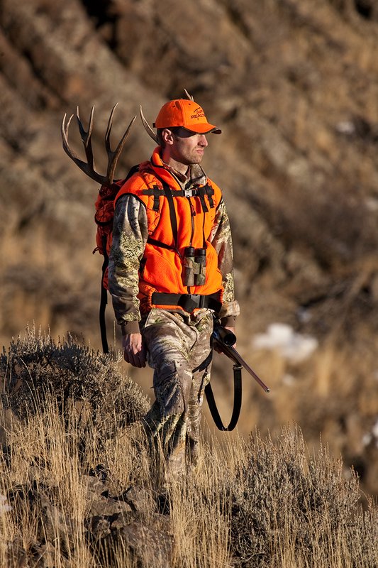 ©TC-Rifle Hunter in Snow-D089999-00849.jpg :: Rifle Hunter wearing Advantage Max1-HD camo with florescent orange hat/vest carrying a backpack with meat and rack of trophy mule deer