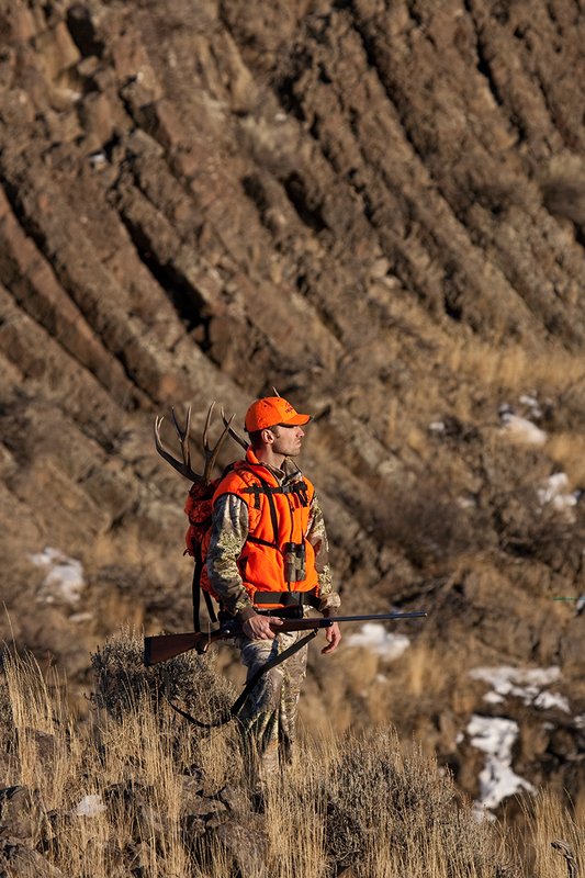 ©TC-Rifle Hunter in Snow-D089999-00858.jpg :: Rifle Hunter wearing Advantage Max1-HD camo with florescent orange hat/vest carrying a backpack with meat and rack of trophy mule deer