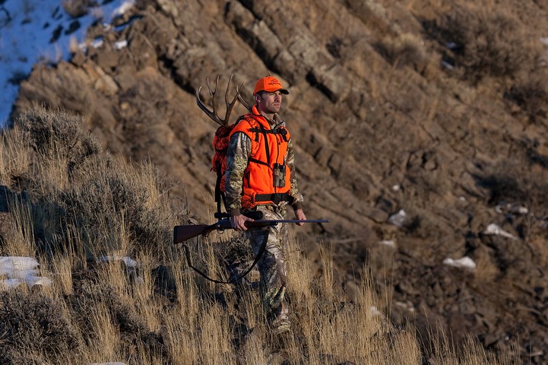©TC-Rifle Hunter in Snow-D089999-00869.jpg :: Rifle Hunter wearing Advantage Max1-HD camo with florescent orange hat/vest carrying a backpack with meat and rack of trophy mule deer