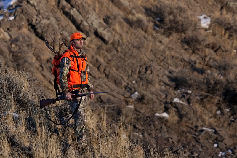 ©TC-Rifle Hunter in Snow-D089999-00873.jpg :: Rifle Hunter wearing Advantage Max1-HD camo with florescent orange hat/vest carrying a backpack with meat and rack of trophy mule deer