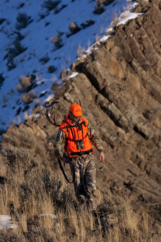 ©TC-Rifle Hunter in Snow-D089999-00879.jpg :: Rifle Hunter wearing Advantage Max1-HD camo with florescent orange hat/vest carrying a backpack with meat and rack of trophy mule deer