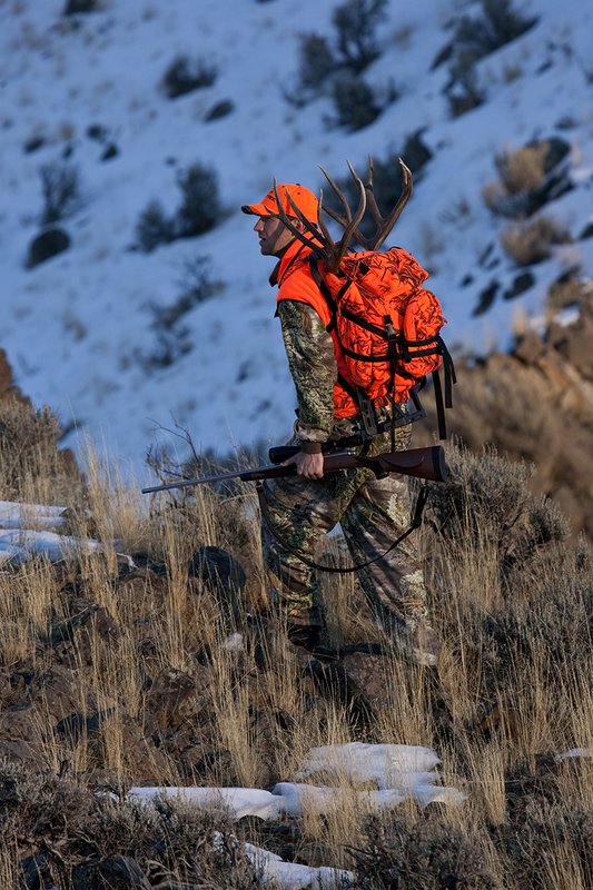 ©TC-Rifle Hunter in Snow-D089999-00882.jpg :: Rifle Hunter wearing Advantage Max1-HD camo with florescent orange hat/vest carrying a backpack with meat and rack of trophy mule deer along sage ridge