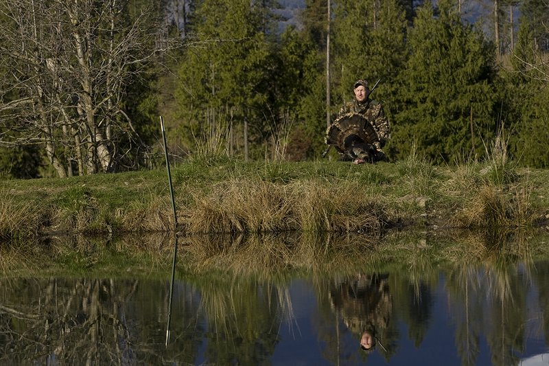 ©TC-Turkey Hunting-D90006-00420.jpg :: Turkey Hunter wearing Advantage Max 4HD Camo admiring his Merriam Long bearded gobbler at edge of pond.  Image of hunter and mountains reflected on surface of the pond.