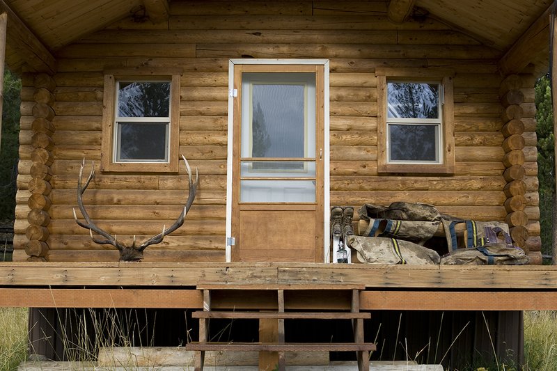 ©TC_Hunting Camps-D80003-116.jpg :: Elk Camp, cabin in woods, with elk rack on porch, panniers for carrying elk quarters, Peet shoe dryer, drying boots after the hunt,
