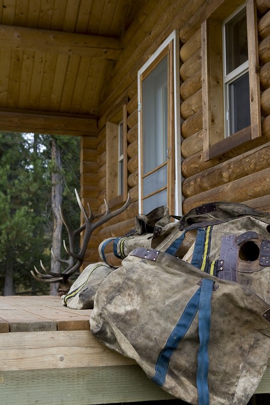 ©TC_Hunting Camps-D80003-123.jpg :: Elk Camp, cabin in woods, with elk rack on porch, panniers for carrying elk quarters, Peet shoe dryer, drying boots after the hunt,