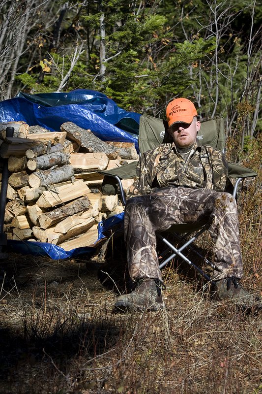 ©TC_Hunting Camps-D80003-141.jpg :: Hunter sitting in lawn chair taking nap in front of wood pile in midday sun, resting from morning of elk hunting