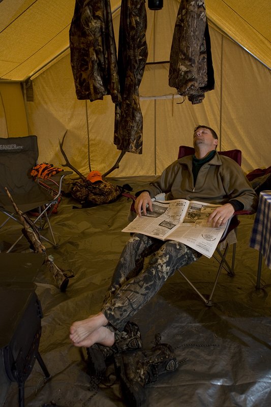©TC_Hunting Camps-D80003-150.jpg :: Hunter sitting on chair inside wall tent, getting warm and drying off after a day of hunting elk