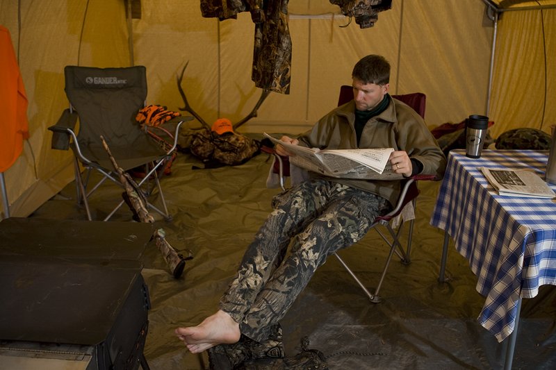 ©TC_Hunting Camps-D80003-153.jpg :: Hunter sitting on chair inside wall tent, getting warm and drying off after a day of hunting elk