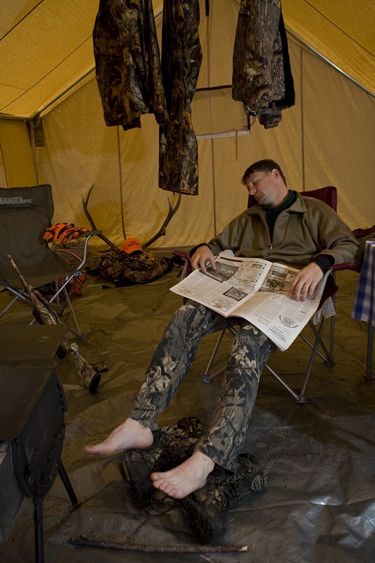 ©TC_Hunting Camps-D80003-157.jpg :: Hunter sitting on chair inside wall tent, getting warm and drying off after a day of hunting elk