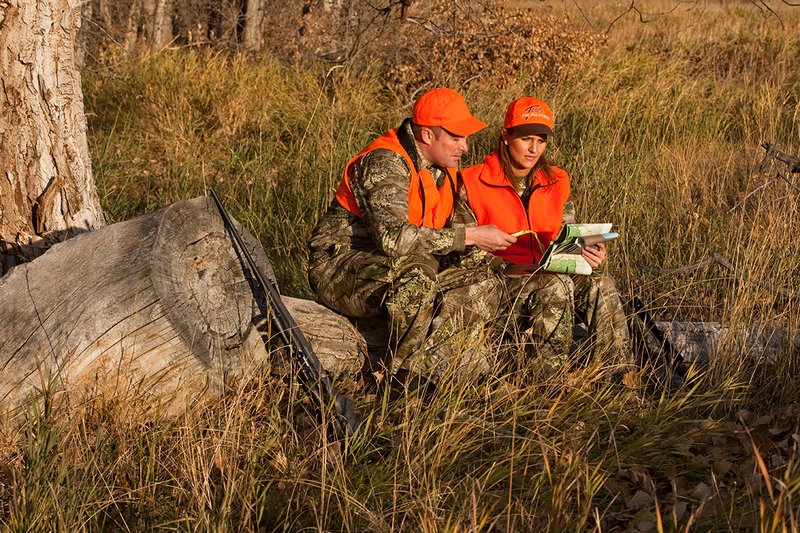 TC-Hunt-Women Big Game-D89992-00302.jpg :: Woman and man rifle hunting, river bottom, cottonwood trees, Max 1 camo, orange vest, hat, Elite Bushnell optics, looking at map, compass, naviagting,
