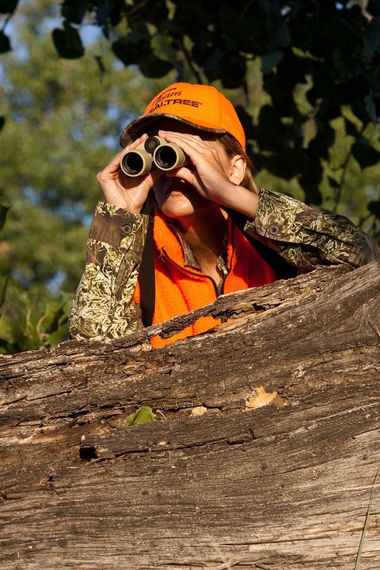 TC-Hunt-Women Big Game-D89992-00394.jpg :: Woman hunter dressed in florescent orange and Advantage Max1-HD camo glasses with Leupold Katmai 6x32 binocular using a Crooked Horn Outfitter slide and flex binocular strap to steady the binocular.
