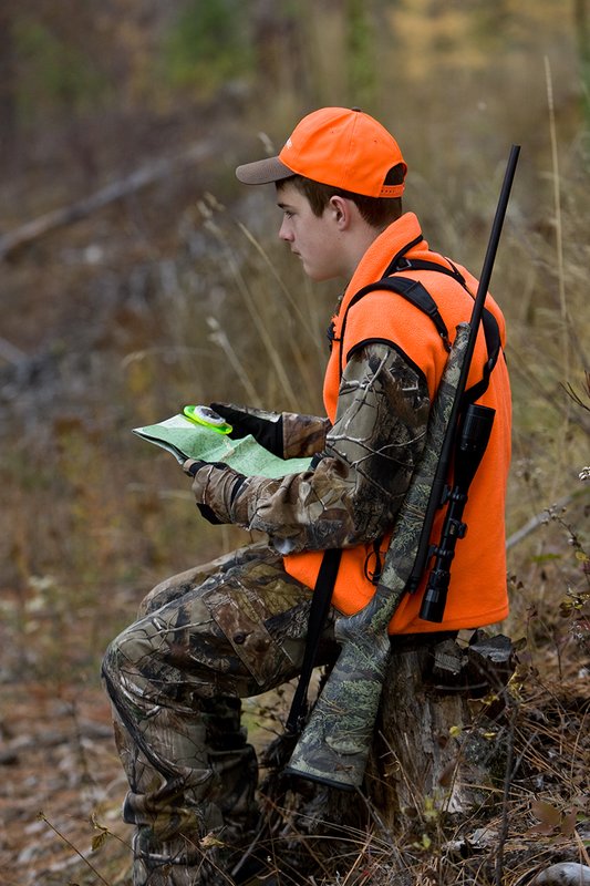 TC-Hunter Parent Child-D89995-00407.jpg :: Teenage boy hunting for big game wearing Advantage AP-Brown Camoflage and an orange vest and ball cap sitting on a stand checking his compass while deer hunting in open timber
