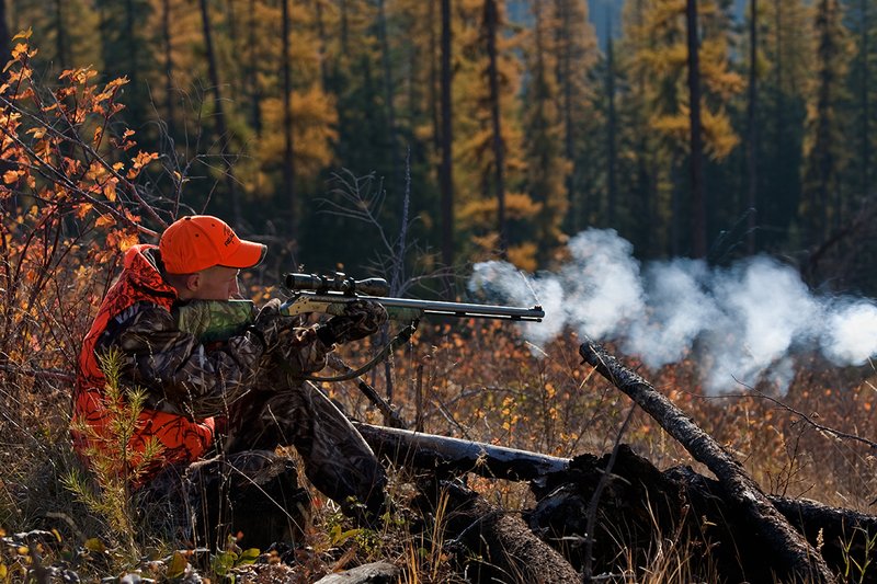 TC-Muzzleloader Hunters-D90008-00350.jpg :: Muzzleloader hunter wearing Advantage Max4-HD camo and Realtree Orange Vest shooting CVA Muzzleloader topped with Leuopold Omega Scope with smoke from muzzleoader coming from barrel, Larch trees in fall colors backlit in background