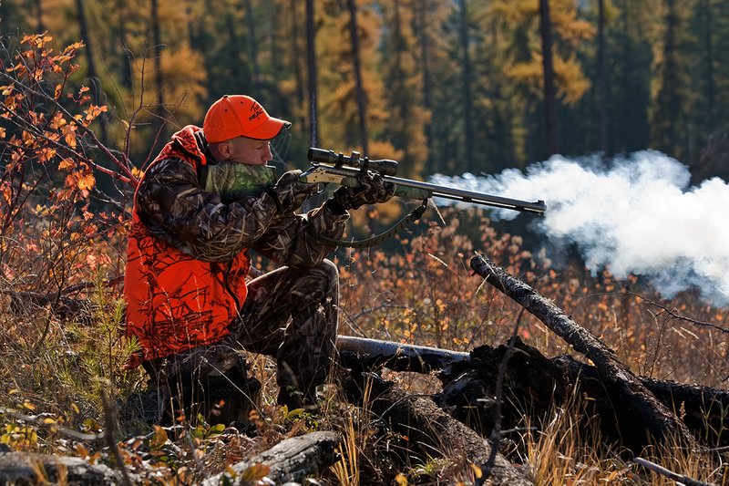 TC-Muzzleloader Hunters-D90008-00353.jpg :: Muzzleloader hunter wearing Advantage Max4-HD camo and Realtree Orange Vest shooting CVA Muzzleloader topped with Leuopold Omega Scope with smoke from muzzleoader coming from barrel, Larch trees in fall colors backlit in background