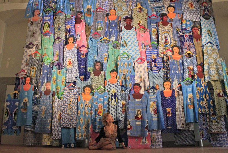 Installation of SHIFT SpoletoJune 2013.jpg :: '' Ownership, identity and hybridization: Virginia Ryan's Shift/Rue de Commerce rotates around these concepts: reinterpreting, from a Western viewpoint, meanings and symbols that are intertwined in the colorful Pagne (wax printed cloths ) widely used in West Africa. Fundamentally ~but not exclusively ~ a woman's story, the cloths can be seen as actual 'semiotic mappings' in which ornamentation is but the most obvious of an iconographic meta~language presenting a world of dreams, hopes, ambition and power. It is not only a female story because the dresses (and elaborate head~dresses) made from the cloths empower the women with a regal beauty in their daily lives, but because it was women,such as the Togolese Nana Benz who created a veritable economic empire in the twentieth century by spreading the commerce in wax prints beyond national borders. To bring into the contemporary art world the history of these prints (which are not originally African, but rather Indonesian, where an ancient tradition of batik for sarongs and other clothing flourished) was the anglo~nigerian artist Yinka Shonibare MBE. With a touch of irony, Shonibare has interpreted this hybridization and in a sense, the disorientation occurring when considering that the material is marked by colonial histories in both a political and cultural sense. Colonial powers : Holland first,followed by Britain, had,by the middle of the 19th century,appropriated Indonesian techniques, used them to catalyze their textile industries before re~exporting to the markets of West Africa. These are the very cloths we, in the West, tend to think of as 'African'. Also in Shift/Rue Du Commerce we discover a strong connection with the story of the 'wax print',but rather than with an ironic gaze Virginia Ryan , born in Australia, intuitively attempts to create order from what may at first appear chaotic, by following the lure of primordial symbols also to be found in Aboriginal cultures. The work is conceived as a dialogue which plays on ambiguity, first and foremost linguistic.The word 'Shift' in English implies movement.But other meanings are also in use , such as the name for the classic dress designed by Coco Chanel in the 1920s, still a cult item. The second part of the title, Rue du Commerce has rather a precise geographic location whilst simultaneously referring back to meanings made more explicit in 'Shift'. Rue du Commerce is born,rather, from the very action of the artist walking with her ever~present camera , her vision already framing the photographic image.Walking along the shopping street of Rue du Commerce in the Plateau area of Abidjan,the artist began photographing the rows of Pagne visible in the boutique windows. 'Revisiting those photographs on the computer screen,where the very image is flattened , I perceived them as being divorced from the initial visual experience\