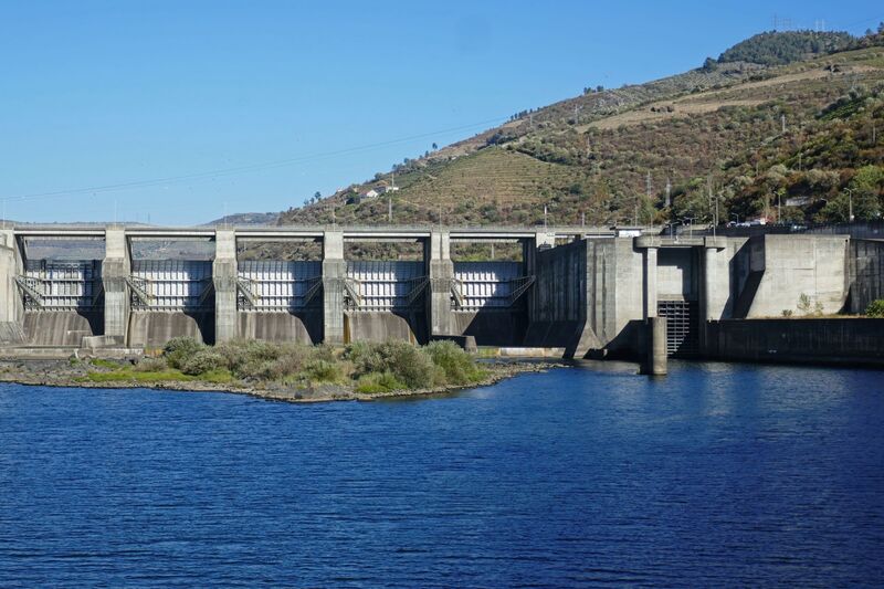 DC 22-0789-031.jpg :: Saga Douro River Cruise, Regua Lamego to Pinhao, River Douro: Régua Dam (Portuguese: Barragem da Régua) is a concrete gravity dam on the Douro, where the river forms the border line between the districts of Vila Real and Viseu. It is located in the municipality Peso da Régua, in Vila Real District. Construction of the dam began in 1965. The dam was completed in 1973. It is owned by Companhia Portuguesa de Produção de Electricidade (CPPE). Photo taken 30/08/2022.