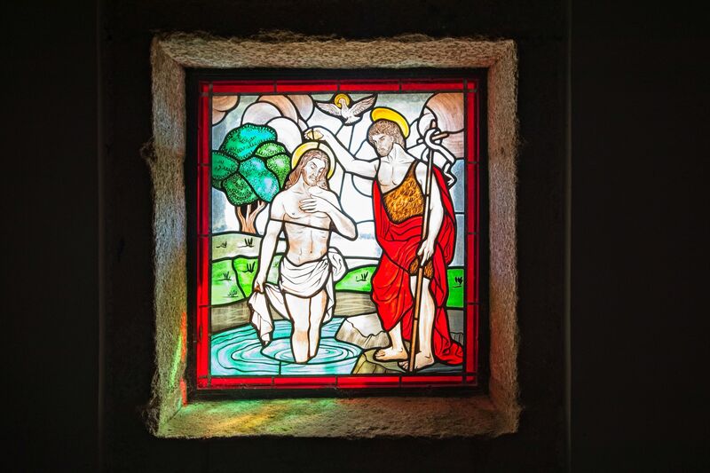 DC 22-0791-073.jpg :: Saga Douro River Cruise, Barca d'Alva, Castelo Rodrigo: The Mother Church is dedicated to Our Lady of Rocamador, and was founded in the thirteenth century by the Confraternity of the Friars of Our Lady of Rocamador, a congregation that was dedicated to assisting Compostela pilgrims. The Property maintains the primitive typology, it is an example of transition between Romanesque and Gothic, but it underwent later works, namely in the sixteenth and seventeenth centuries, which changed the structure of the temple. It has a composite plan, three naves, straight lintel porticoes and angular pediment. Inside we can admire a wooden coffered ceiling painted with hagiographic scenes, in the chancel eighteenth-century blue and white tiles and in the main altar Hispano-Arabic tiles. The Church was restored in the late 90s as part of the Historical Villages of Portugal Program. P.s Stained glass window showing John the Baptist pouring water over Jesus's head while a dove, symbolizing the Holy Spirit, descends from above. Photo taken 31/08/2022