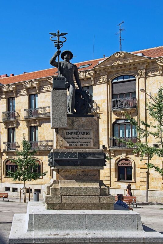 DC 22-0794-024.jpg :: Saga Douro River Cruise, Salamanca. Spain: This is the Monumento al Empresario (Monument to the Businessman) in Salamanca. The monument is located on the Gran Vía in Salamanca. It was created by the sculptor Gabriel Sánchez Calzada. The text on the pedestal refers to the Salamanca Official Chamber of Commerce (Cámara Oficial de Comercio) and the years 1886-1986. The figure holds a caduceus, a symbol often associated with commerce and negotiation. The bronze sculpture depicts the Roman god Mercury (Hermes in Greek mythology), who is considered the god of commerce, among other things. He is shown holding a caduceus, his traditional symbol, and wearing a hat. Photo taken 01/09/2022