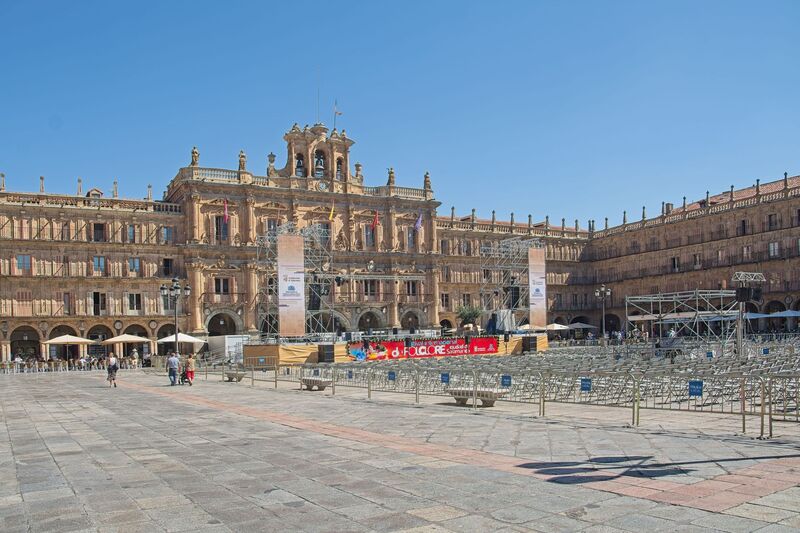 DC 22-0794-027.jpg :: Saga Douro River Cruise, Salamanca. Spain: The famous Plaza Mayor in Salamanca. Widely considered one of the most beautiful squares in the country, it is a significant example of Spanish Baroque architecture built in the 18th century. The Plaza Mayor is in the heart of Salamanca, a pedestrianized area that serves as the city's main social hub. It was primarily designed by architect Alberto Churriguera and completed in 1755. The buildings feature a uniform design of three stories, with arcades lining the perimeter and medallions depicting historic figures above the arches. Historically used for markets, bullfights, and public ceremonies, today the square is lined with numerous shops, restaurants, and cafes. It frequently hosts local events, concerts, and festivals, which explains the stage and seating setup. Photo taken 01/09/2022