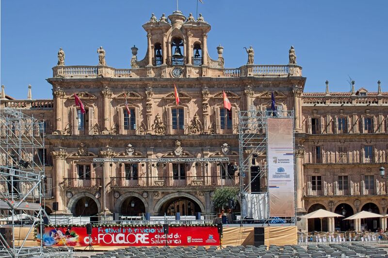 DC 22-0794-030.jpg :: Saga Douro River Cruise, Salamanca. Spain: The famous Plaza Mayor in Salamanca. Widely considered one of the most beautiful squares in the country, it is a significant example of Spanish Baroque architecture built in the 18th century. The Plaza Mayor is in the heart of Salamanca, a pedestrianized area that serves as the city's main social hub. It was primarily designed by architect Alberto Churriguera and completed in 1755. The buildings feature a uniform design of three stories, with arcades lining the perimeter and medallions depicting historic figures above the arches. Historically used for markets, bullfights, and public ceremonies, today the square is lined with numerous shops, restaurants, and cafes. It frequently hosts local events, concerts, and festivals, which explains the stage and seating setup. Photo taken 01/09/2022