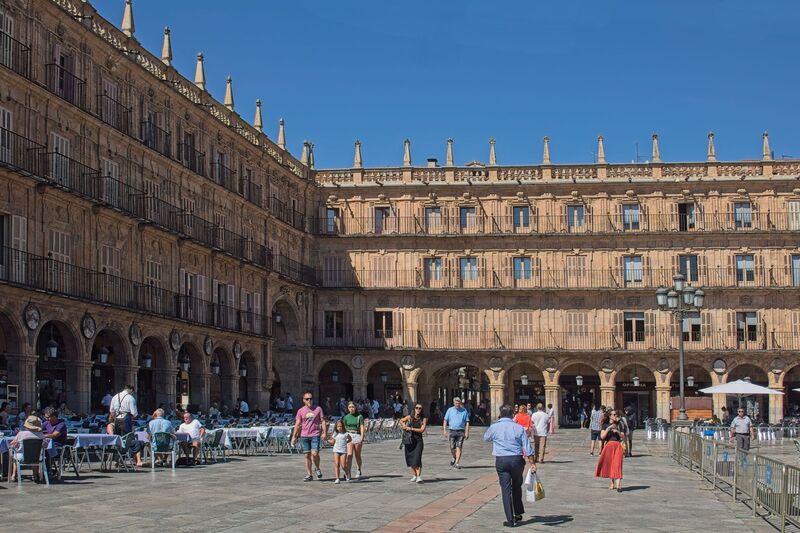 DC 22-0794-033.jpg :: Saga Douro River Cruise, Salamanca. Spain: The famous Plaza Mayor in Salamanca. Widely considered one of the most beautiful squares in the country, it is a significant example of Spanish Baroque architecture built in the 18th century. The Plaza Mayor is in the heart of Salamanca, a pedestrianized area that serves as the city's main social hub. It was primarily designed by architect Alberto Churriguera and completed in 1755. The buildings feature a uniform design of three stories, with arcades lining the perimeter and medallions depicting historic figures above the arches. Historically used for markets, bullfights, and public ceremonies, today the square is lined with numerous shops, restaurants, and cafes. It frequently hosts local events, concerts, and festivals, which explains the stage and seating setup. Photo taken 01/09/2022