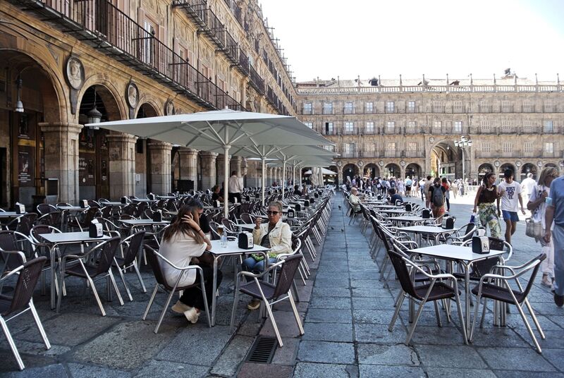 DC 22-0794-036.jpg :: Saga Douro River Cruise, Salamanca. Spain: The famous Plaza Mayor in Salamanca. Widely considered one of the most beautiful squares in the country, it is a significant example of Spanish Baroque architecture built in the 18th century. The Plaza Mayor is in the heart of Salamanca, a pedestrianized area that serves as the city's main social hub. It was primarily designed by architect Alberto Churriguera and completed in 1755. The buildings feature a uniform design of three stories, with arcades lining the perimeter and medallions depicting historic figures above the arches. Historically used for markets, bullfights, and public ceremonies, today the square is lined with numerous shops, restaurants, and cafes. It frequently hosts local events, concerts, and festivals, which explains the stage and seating setup. Photo taken 01/09/2022