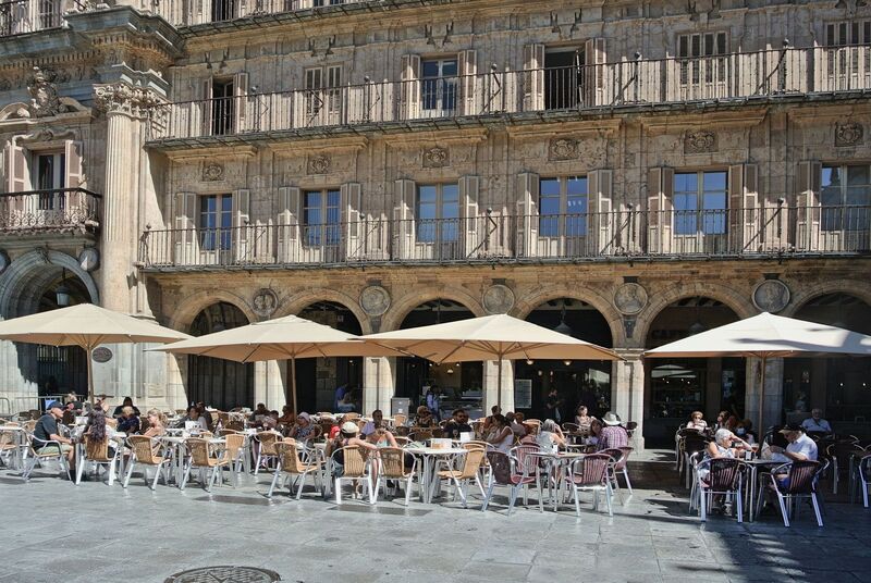 DC 22-0794-037.jpg :: Saga Douro River Cruise, Salamanca. Spain: The famous Plaza Mayor in Salamanca. Widely considered one of the most beautiful squares in the country, it is a significant example of Spanish Baroque architecture built in the 18th century. The Plaza Mayor is in the heart of Salamanca, a pedestrianized area that serves as the city's main social hub. It was primarily designed by architect Alberto Churriguera and completed in 1755. The buildings feature a uniform design of three stories, with arcades lining the perimeter and medallions depicting historic figures above the arches. Historically used for markets, bullfights, and public ceremonies, today the square is lined with numerous shops, restaurants, and cafes. It frequently hosts local events, concerts, and festivals, which explains the stage and seating setup. Photo taken 01/09/2022