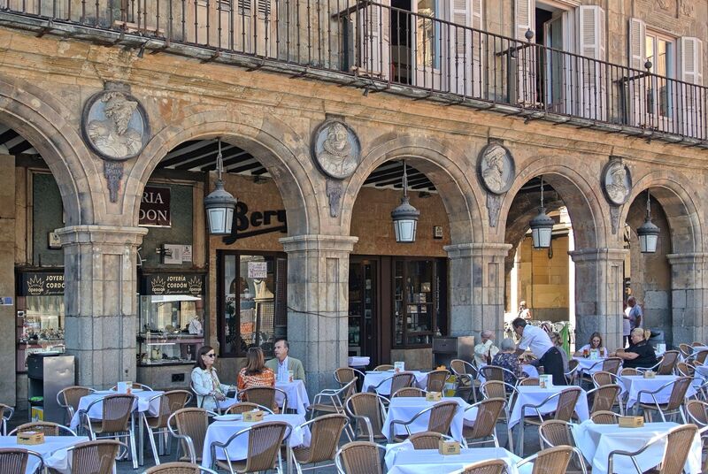 DC 22-0794-038.jpg :: Saga Douro River Cruise, Salamanca. Spain: The famous Plaza Mayor in Salamanca. Widely considered one of the most beautiful squares in the country, it is a significant example of Spanish Baroque architecture built in the 18th century. The Plaza Mayor is in the heart of Salamanca, a pedestrianized area that serves as the city's main social hub. It was primarily designed by architect Alberto Churriguera and completed in 1755. The buildings feature a uniform design of three stories, with arcades lining the perimeter and medallions depicting historic figures above the arches. Historically used for markets, bullfights, and public ceremonies, today the square is lined with numerous shops, restaurants, and cafes. It frequently hosts local events, concerts, and festivals, which explains the stage and seating setup. Photo taken 01/09/2022