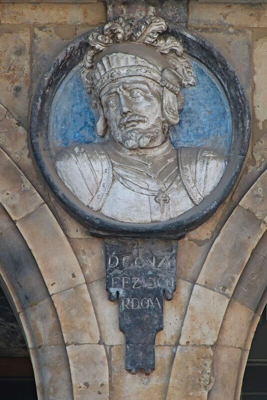 DC 22-0794-043.jpg :: Saga Douro River Cruise, Salamanca. Spain: he famous Plaza Mayor in Salamanca. Widely considered one of the most beautiful squares in the country, it is a significant example of Spanish Baroque architecture built in the 18th century. The Plaza Mayor is in the heart of Salamanca, a pedestrianized area that serves as the city's main social hub. It was primarily designed by architect Alberto Churriguera and completed in 1755. The buildings feature a uniform design of three stories, with arcades lining the perimeter and medallions depicting historic figures above the arches. Historically used for markets, bullfights, and public ceremonies, today the square is lined with numerous shops, restaurants, and cafes. It frequently hosts local events, concerts, and festivals, which explains the stage and seating setup. This medallion features a carving of Gonzalo Fernández de Córdoba, known as \