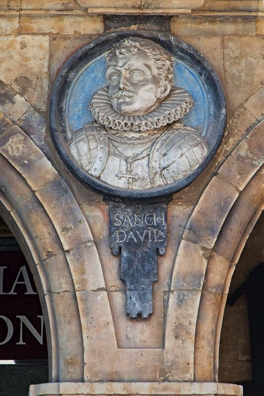 DC 22-0794-045.jpg :: Saga Douro River Cruise, Salamanca. Spain: he famous Plaza Mayor in Salamanca. Widely considered one of the most beautiful squares in the country, it is a significant example of Spanish Baroque architecture built in the 18th century. The Plaza Mayor is in the heart of Salamanca, a pedestrianized area that serves as the city's main social hub. It was primarily designed by architect Alberto Churriguera and completed in 1755. The buildings feature a uniform design of three stories, with arcades lining the perimeter and medallions depicting historic figures above the arches. Historically used for markets, bullfights, and public ceremonies, today the square is lined with numerous shops, restaurants, and cafes. It frequently hosts local events, concerts, and festivals, which explains the stage and seating setup. This medallion depicts Sancho Dávila y Daza, a Spanish general also known as \