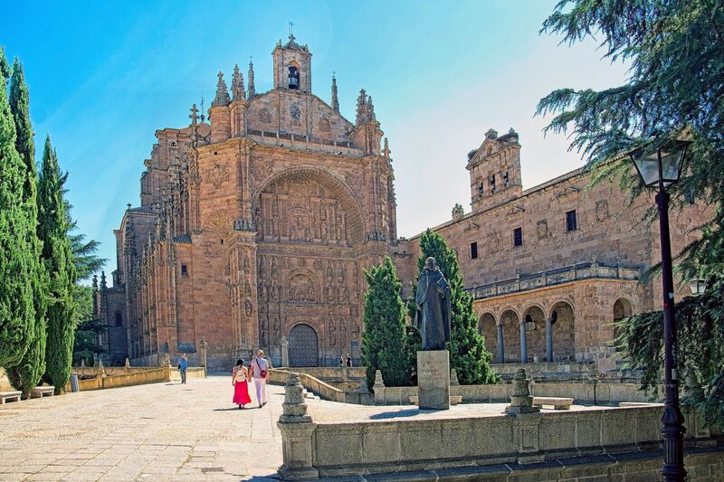 DC 22-0794-047.jpg :: Saga Douro River Cruise, Salamanca. Spain: The image shows the Convent of San Esteban (St. Stephen) in Salamanca. It is a Dominican monastery with a mix of Gothic, Renaissance, and Baroque architectural styles. The most notable feature is the ornate Plateresque facade of the church, which resembles intricate silversmith's work and forms a triumphal arch. The interior contains a magnificent Baroque altarpiece by José de Churriguera. The convent is a repository of significant history. Christopher Columbus is traditionally believed to have stayed at the previous building on the site while seeking support for his voyages from university geographers. It was an important centre for the Dominican fathers who founded the influential School of Salamanca, including Francisco de Vitoria, considered a founding father of international law. The bronze statue in the foreground is a monument to Francisco de Vitoria. Photo taken 01/09/2022