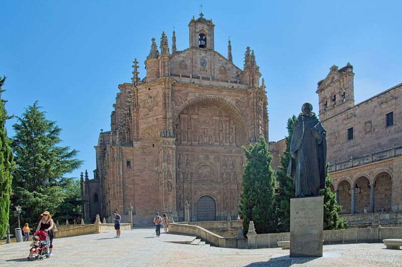 DC 22-0794-048.jpg :: Saga Douro River Cruise, Salamanca. Spain: The image shows the Convent of San Esteban (St. Stephen) in Salamanca. It is a Dominican monastery with a mix of Gothic, Renaissance, and Baroque architectural styles. The most notable feature is the ornate Plateresque facade of the church, which resembles intricate silversmith's work and forms a triumphal arch. The interior contains a magnificent Baroque altarpiece by José de Churriguera. The convent is a repository of significant history. Christopher Columbus is traditionally believed to have stayed at the previous building on the site while seeking support for his voyages from university geographers. It was an important centre for the Dominican fathers who founded the influential School of Salamanca, including Francisco de Vitoria, considered a founding father of international law. The bronze statue in the foreground is a monument to Francisco de Vitoria. Photo taken 01/09/2022